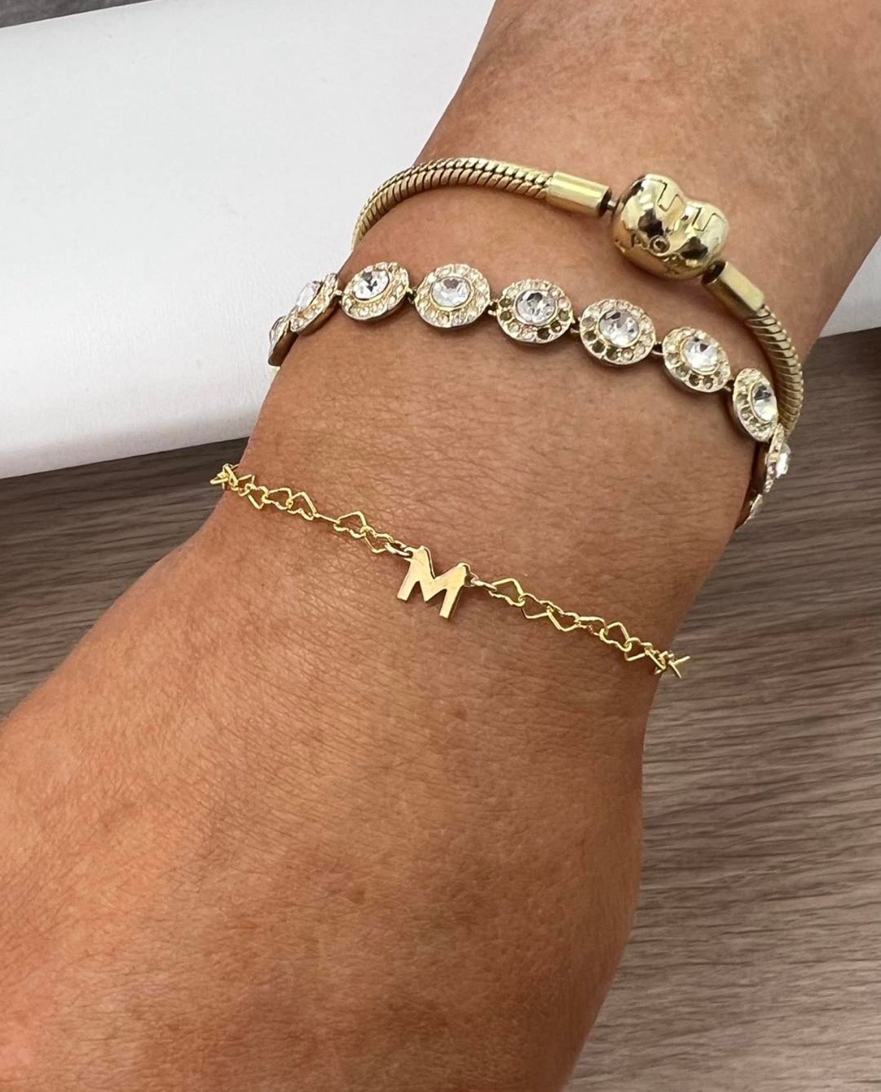 Gold bracelet with decorative elements on a wrist against a neutral background
